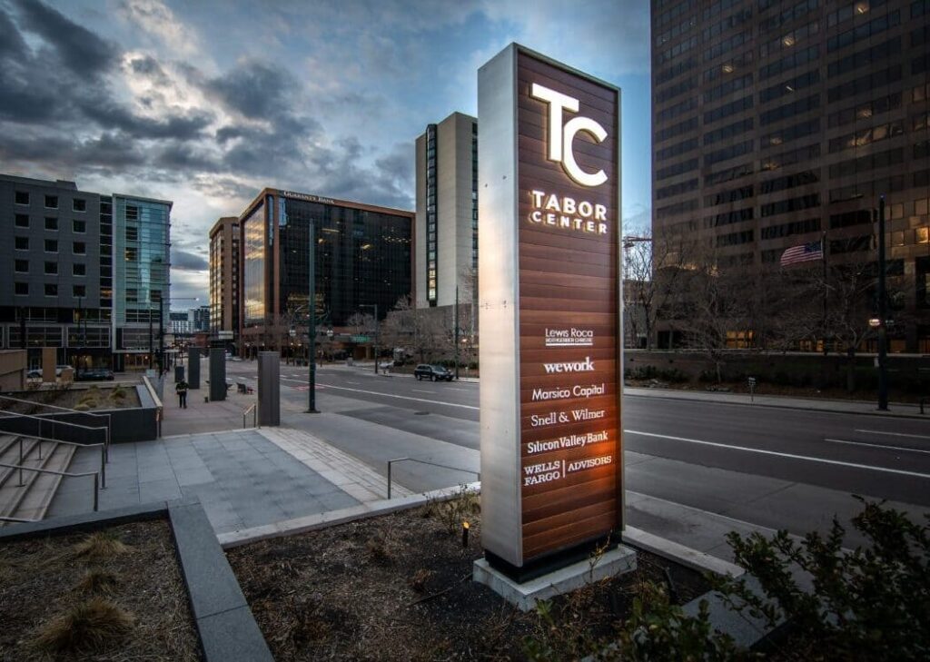 481921020_1426537821966211_7497509960152366926_n-1-e1748975915639 | BSC Signs Illuminated Sign Design for the TC Tabor Center displayed on a city street, featuring prominent branding and high visibility against a backdrop of modern office buildings.. Tall, illuminated sign reading'TC Tabor Center' on a city street with modern office buildings in the background.