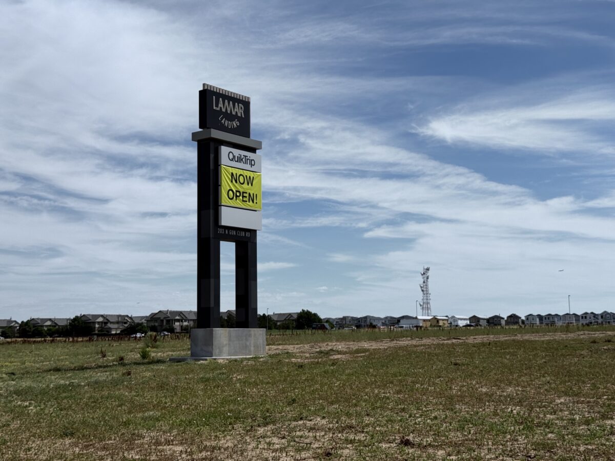 Tall signpost for Lamar Landing and QuikTrip, with a bright yellow Now Open banner against a blue sky.